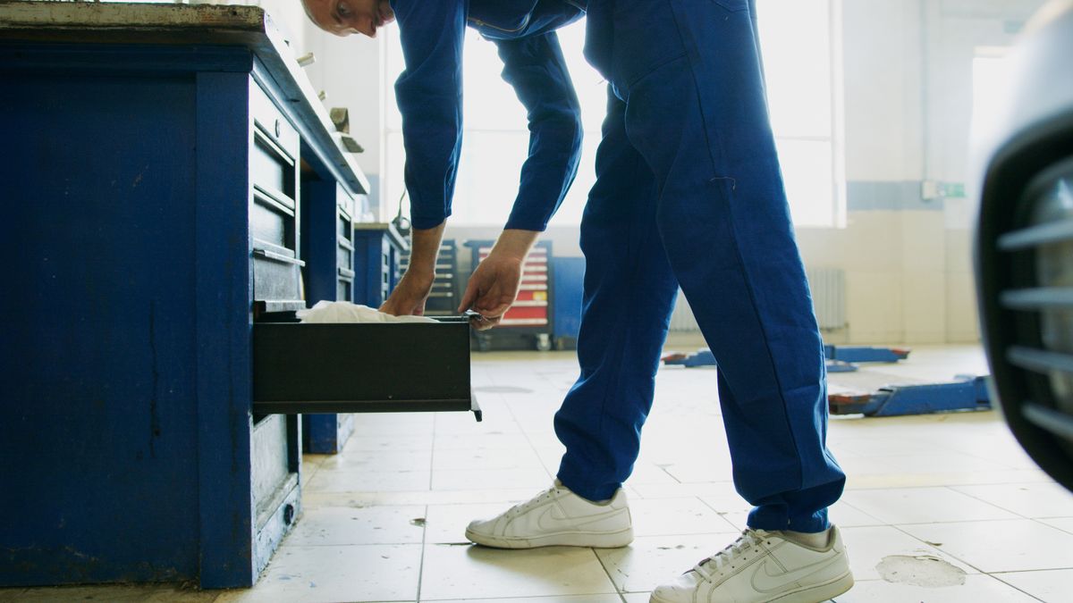 Technician in coveralls opening a tool chest drawer in a repair workshop